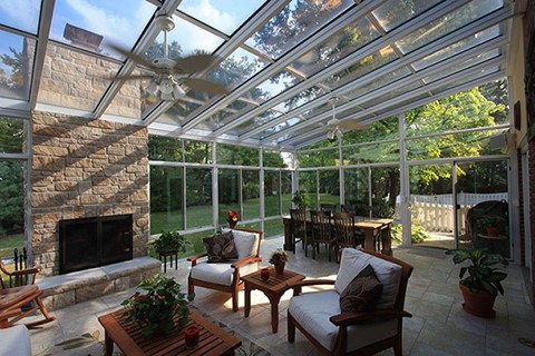 Interior of a Sunroom with a Dining Room Table, Outdoor Chairs and a Coffee Table, and a Fireplace with Ceiling Fans Overhead